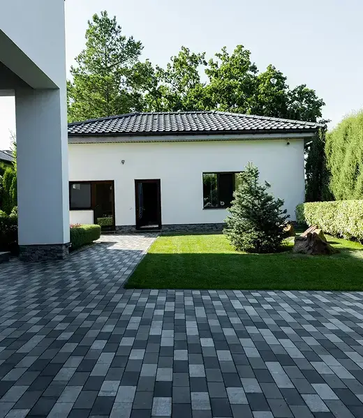 Modern home with a dark gray paver driveway and landscaped front yard